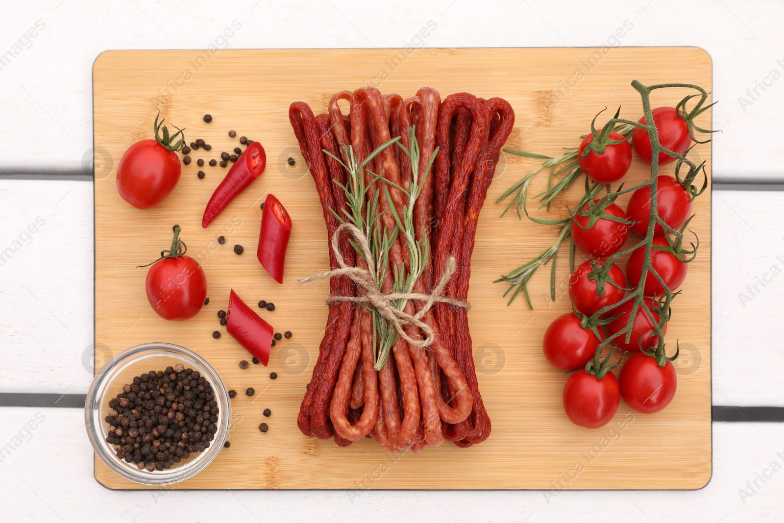 Photo of Bundle of delicious kabanosy with peppercorn, chilli, tomatoes and rosemary on white wooden table, top view