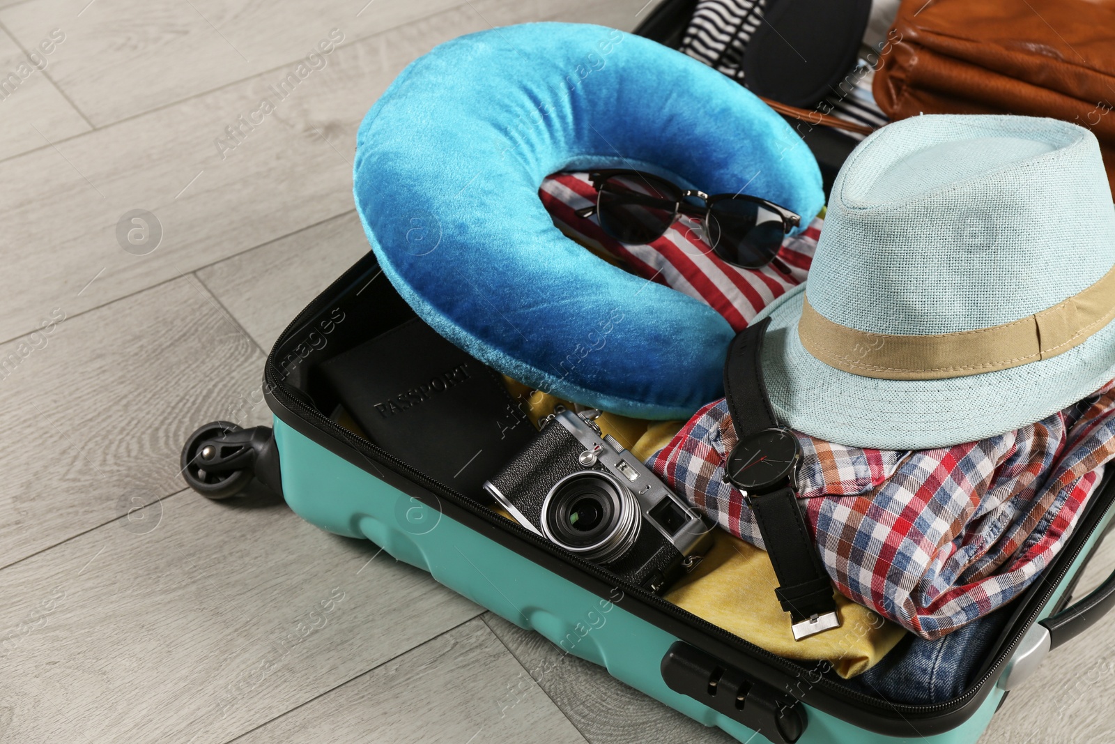 Photo of Opened suitcase with travel pillow and clothes on wooden floor