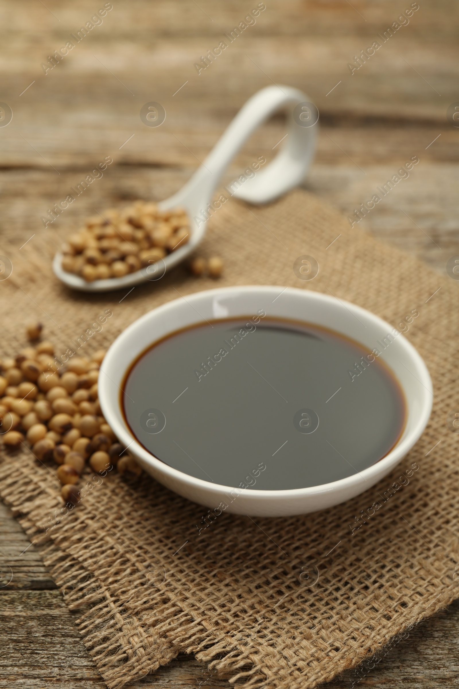 Photo of Soy sauce in bowl and beans on wooden table, closeup