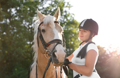 Photo of Young woman in horse riding suit and her beautiful pet outdoors on sunny day