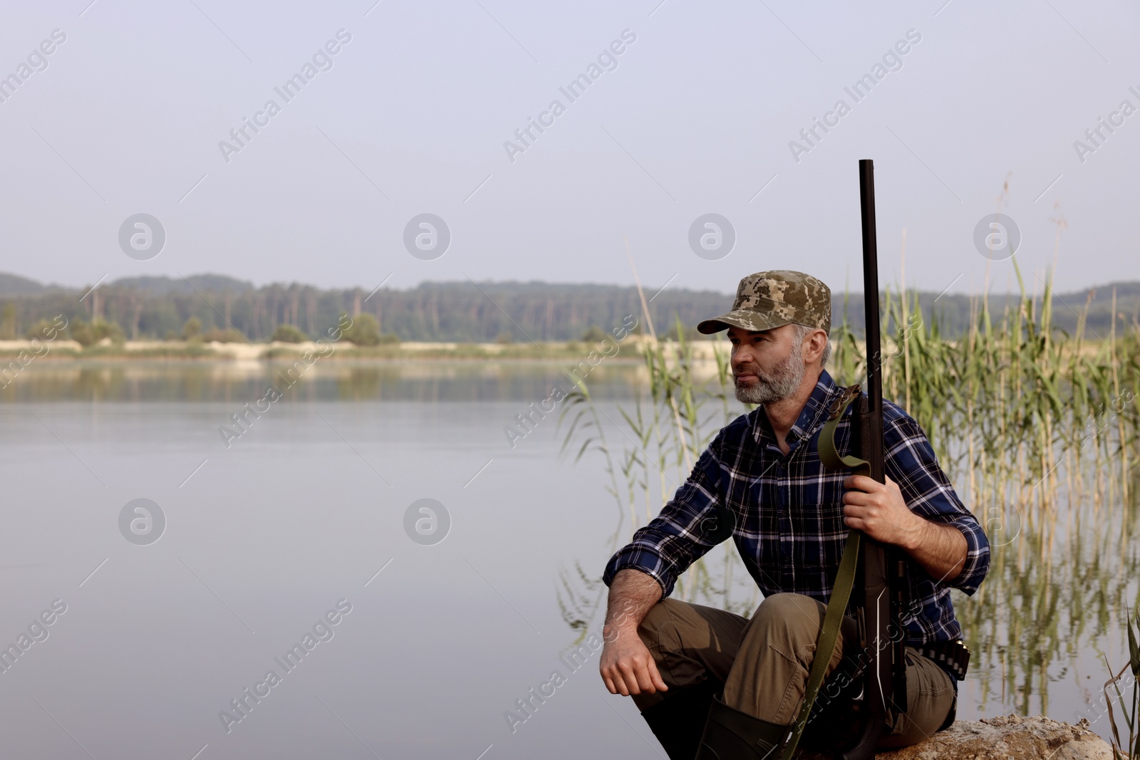 Photo of Man with hunting rifle near lake outdoors. Space for text