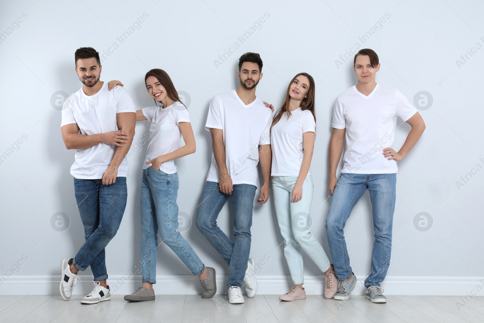 Photo of Group of young people in stylish jeans near light wall