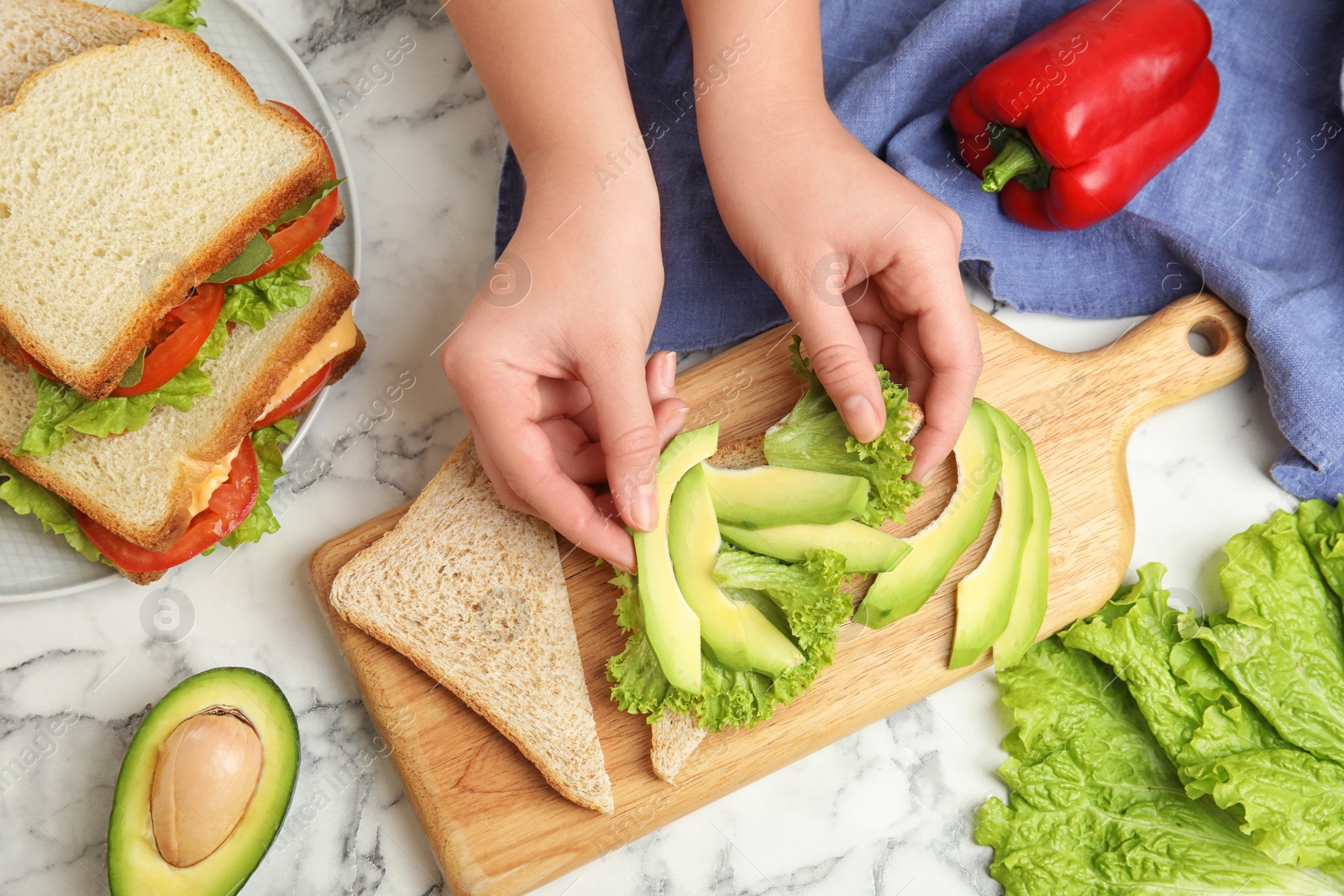 Photo of Woman making tasty sandwich with avocado on white marble table, top view