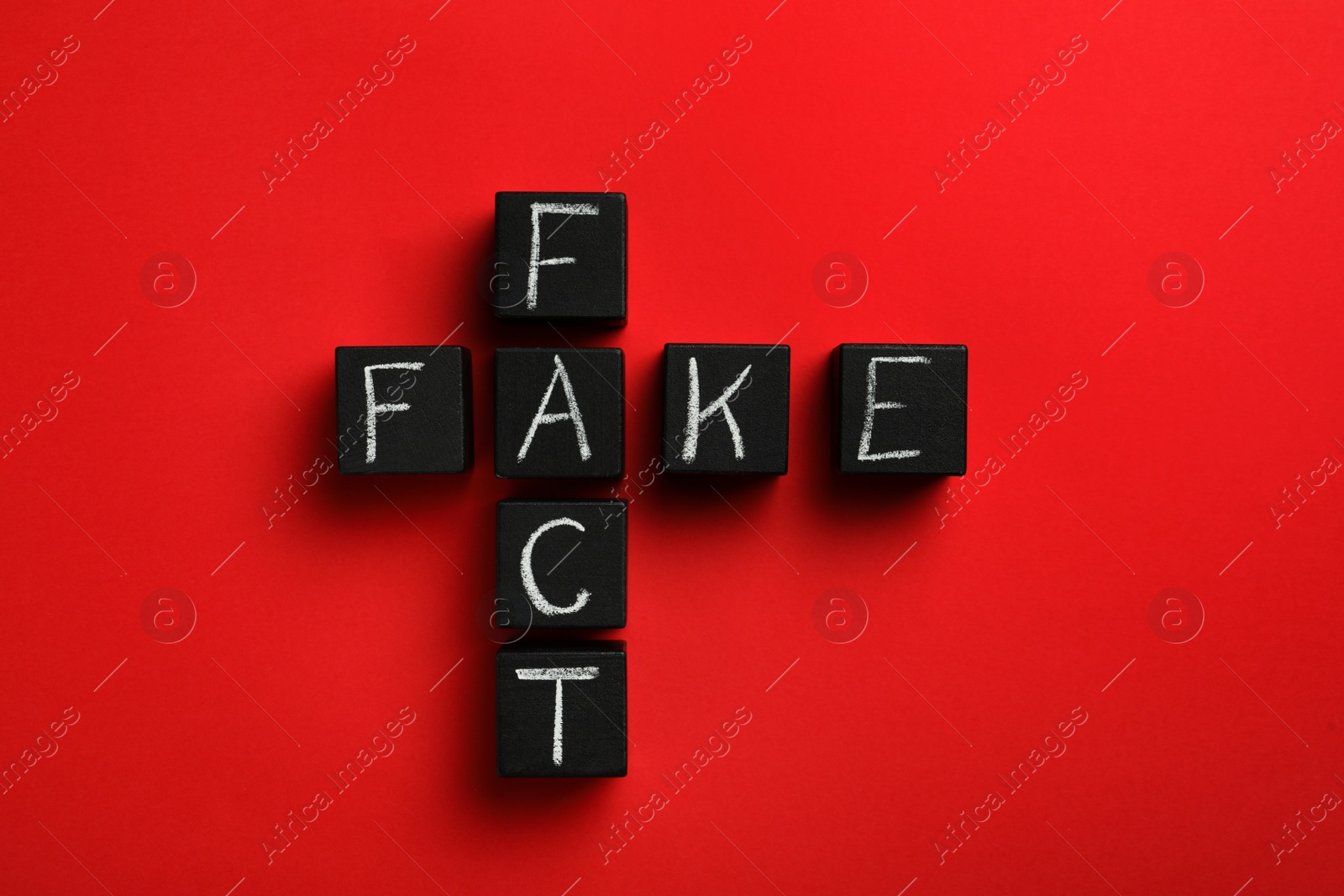 Photo of Words FAKE and FACT made with black cubes on red background, flat lay
