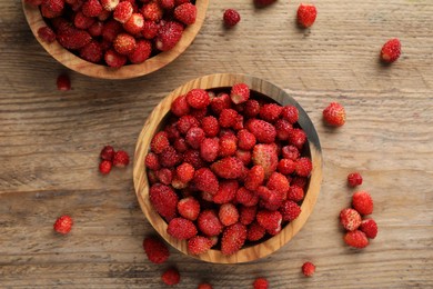 Fresh wild strawberries in bowls on wooden table, flat lay