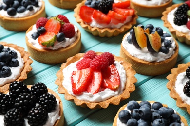 Photo of Many different berry tarts on blue wooden table. Delicious pastries