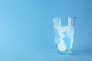 Photo of Glass of water with effervescent tablet on light blue background, space for text