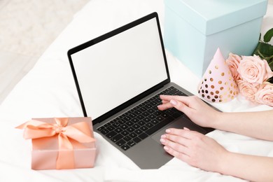 Photo of Woman using laptop near gift and rose flowers on bed in room, closeup. Happy Birthday