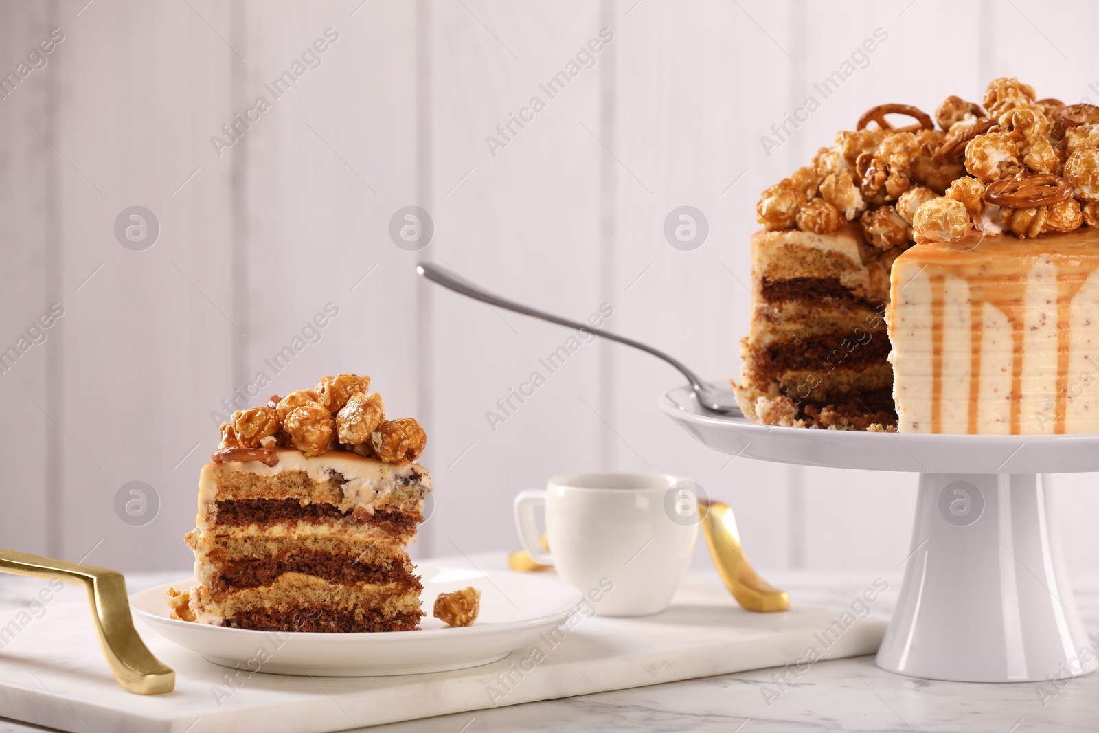 Photo of Caramel drip cake decorated with popcorn and pretzels served on white marble table