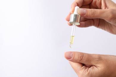 Woman applying cosmetic serum onto her finger on white background, closeup. Space for text