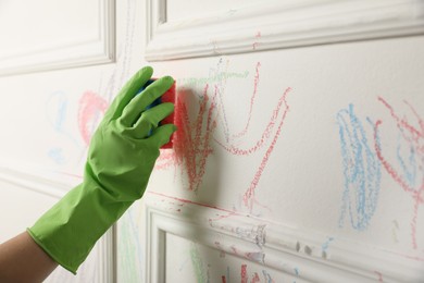 Woman erasing child's drawing from white wall, closeup