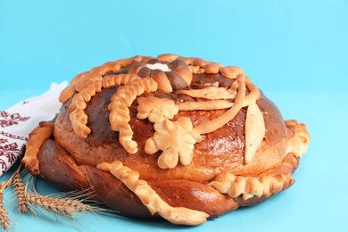 Photo of Rushnyk with korovai on light blue background, closeup. Ukrainian bread and salt welcoming tradition