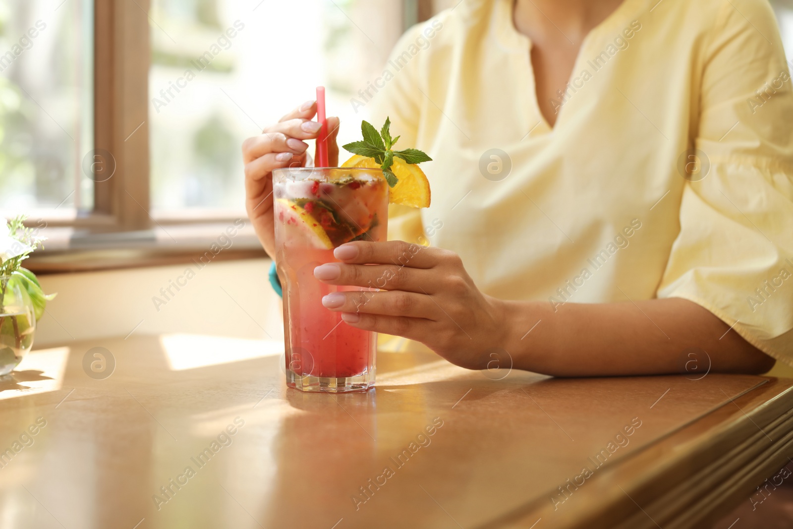 Photo of Young woman with glass of tasty natural lemonade in cafe, closeup. Detox drink