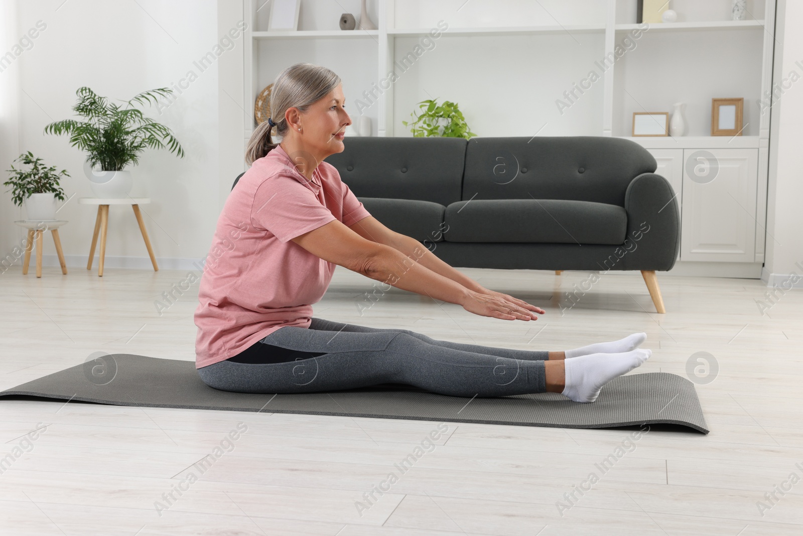 Photo of Senior woman in sportswear stretching on fitness mat at home