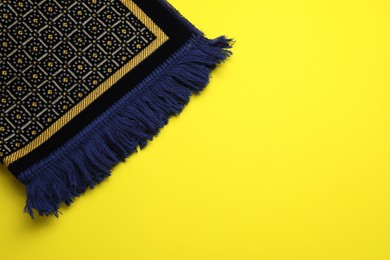 Muslim prayer rug on yellow background, top view. Space for text