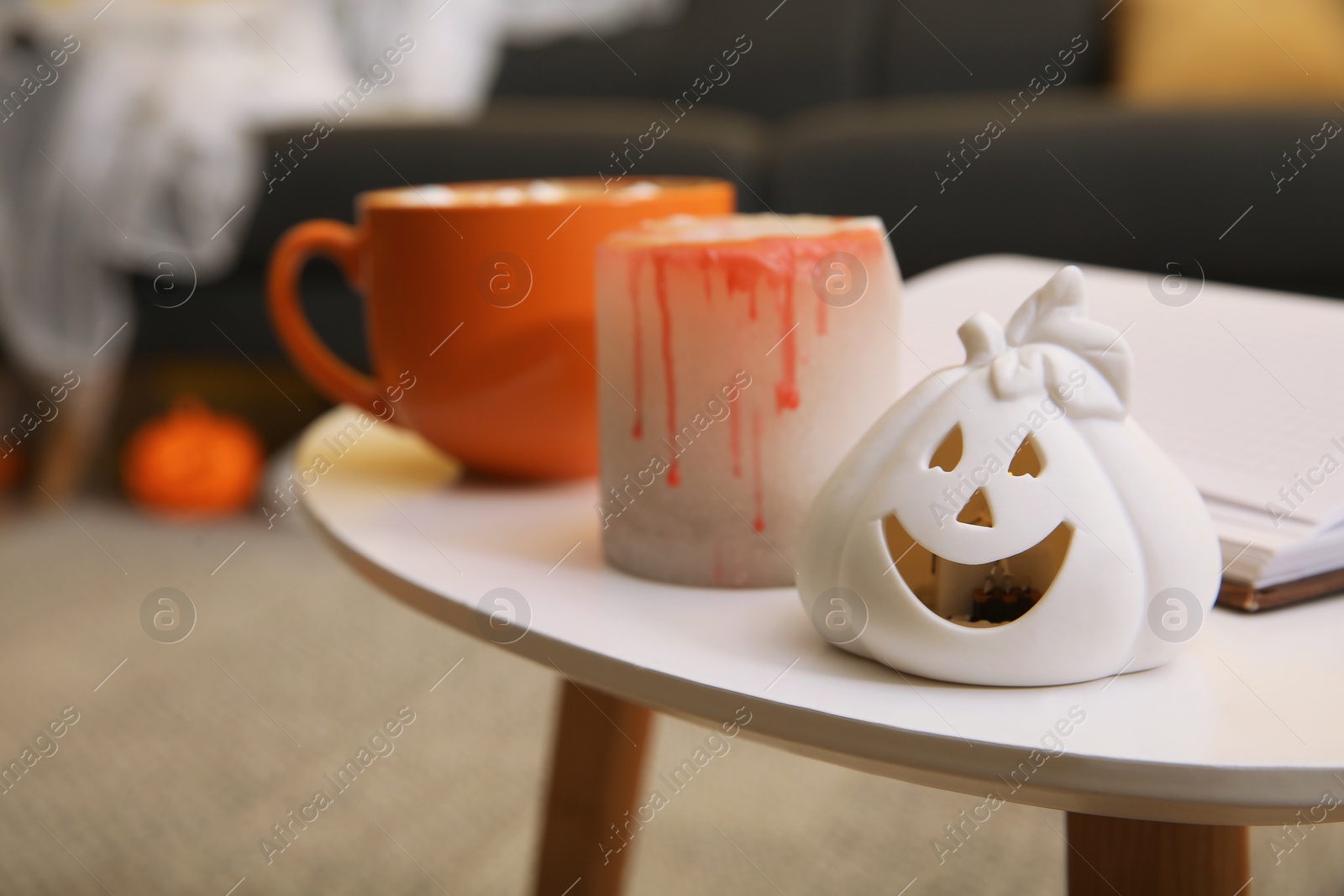 Photo of Halloween decor and cup of delicious drink on white table in room