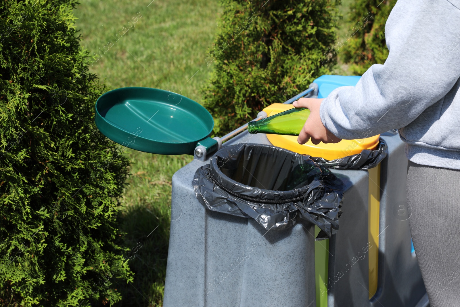 Photo of Woman throwing glass bottle in bin outdoors, closeup. Recycling concept