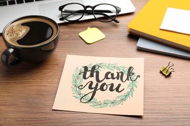 Photo of Card with phrase Thank You, laptop, glasses and notebooks on wooden table