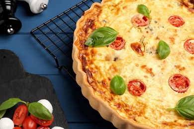 Photo of Delicious quiche with mozzarella cheese, tomatoes and basil on blue wooden table, closeup