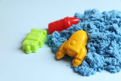 Photo of Bright kinetic sand and plastic toys on light blue background, space for text