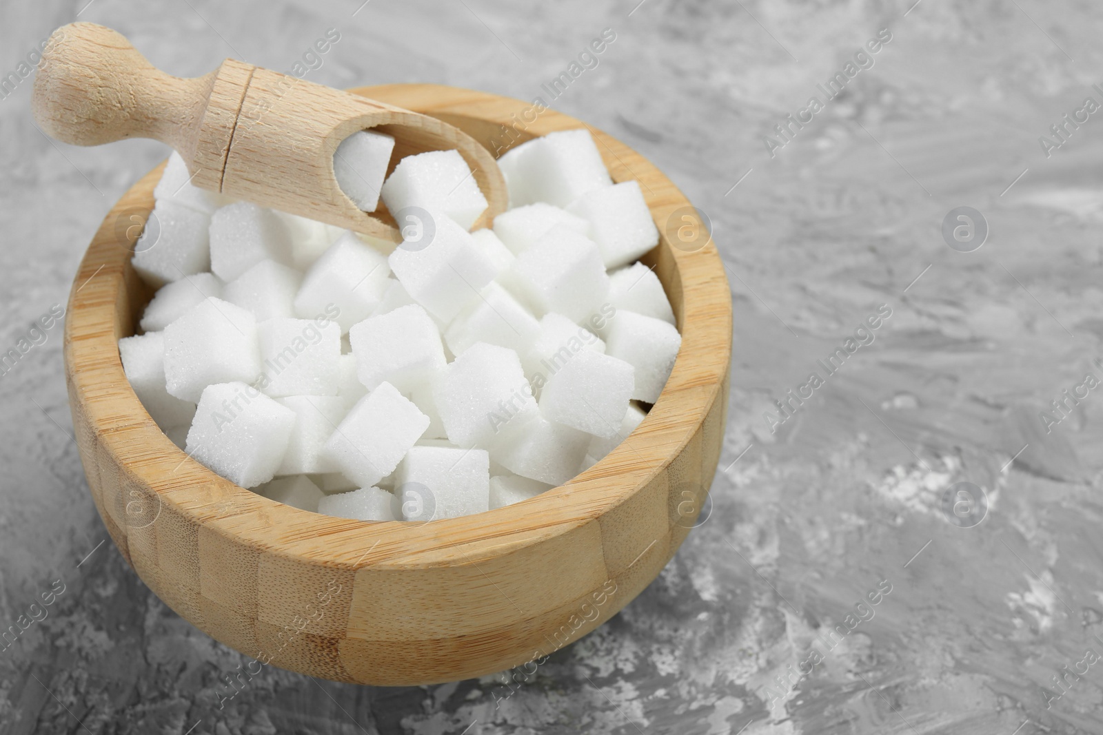 Photo of White sugar cubes in wooden bowl and scoop on grey table. Space for text