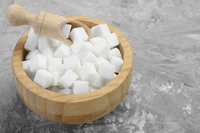 Photo of White sugar cubes in wooden bowl and scoop on grey table. Space for text