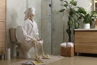 Photo of Skeleton in bathrobe with mobile phone sitting on toilet bowl