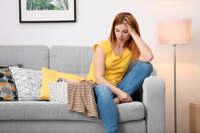 Photo of Tired housewife with laundry sitting on sofa at home