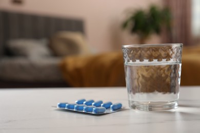 Photo of Glass of water and pills on white table indoors, space for text. Potency problem concept