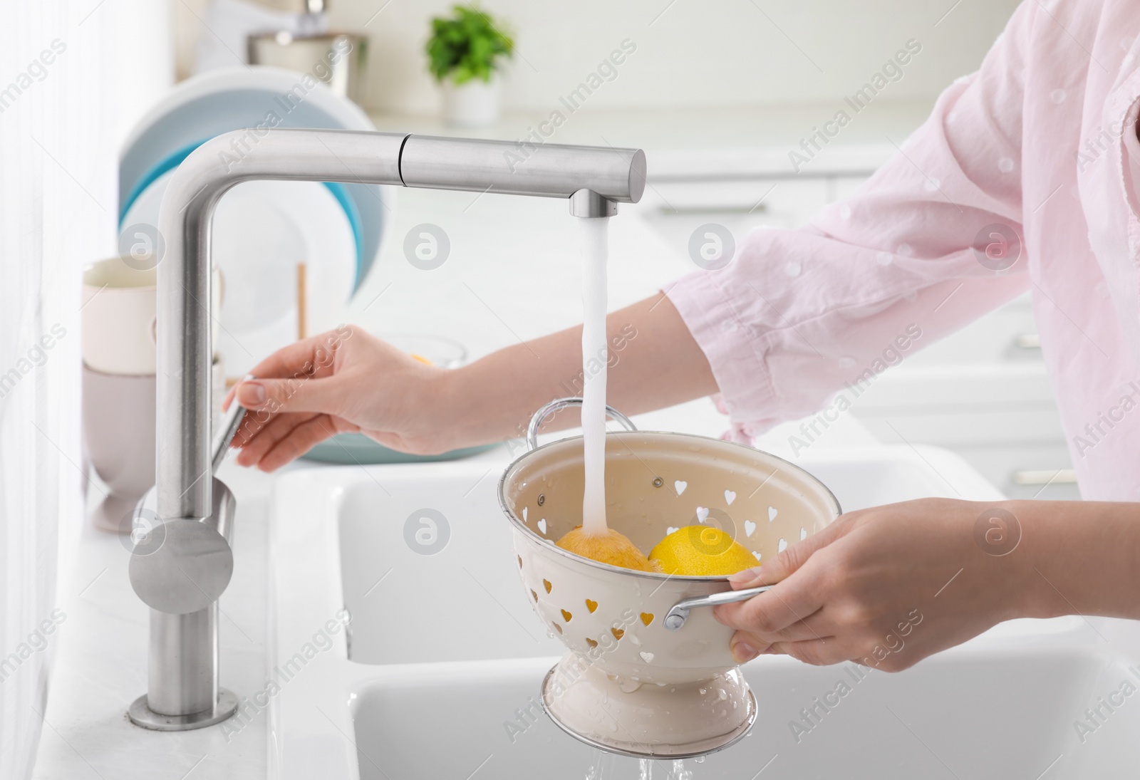 Photo of Woman washing fresh ripe lemons under tap water in kitchen, closeup