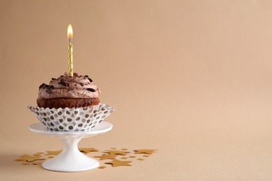 Chocolate cupcake with burning candle on beige background. Space for text