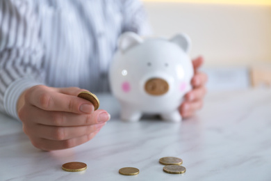 Photo of Woman with piggy bank and coin at marble table indoors, closeup