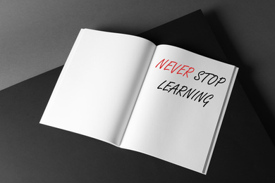 Image of Open book with phrase NEVER STOP LEARNING on dark background, above view