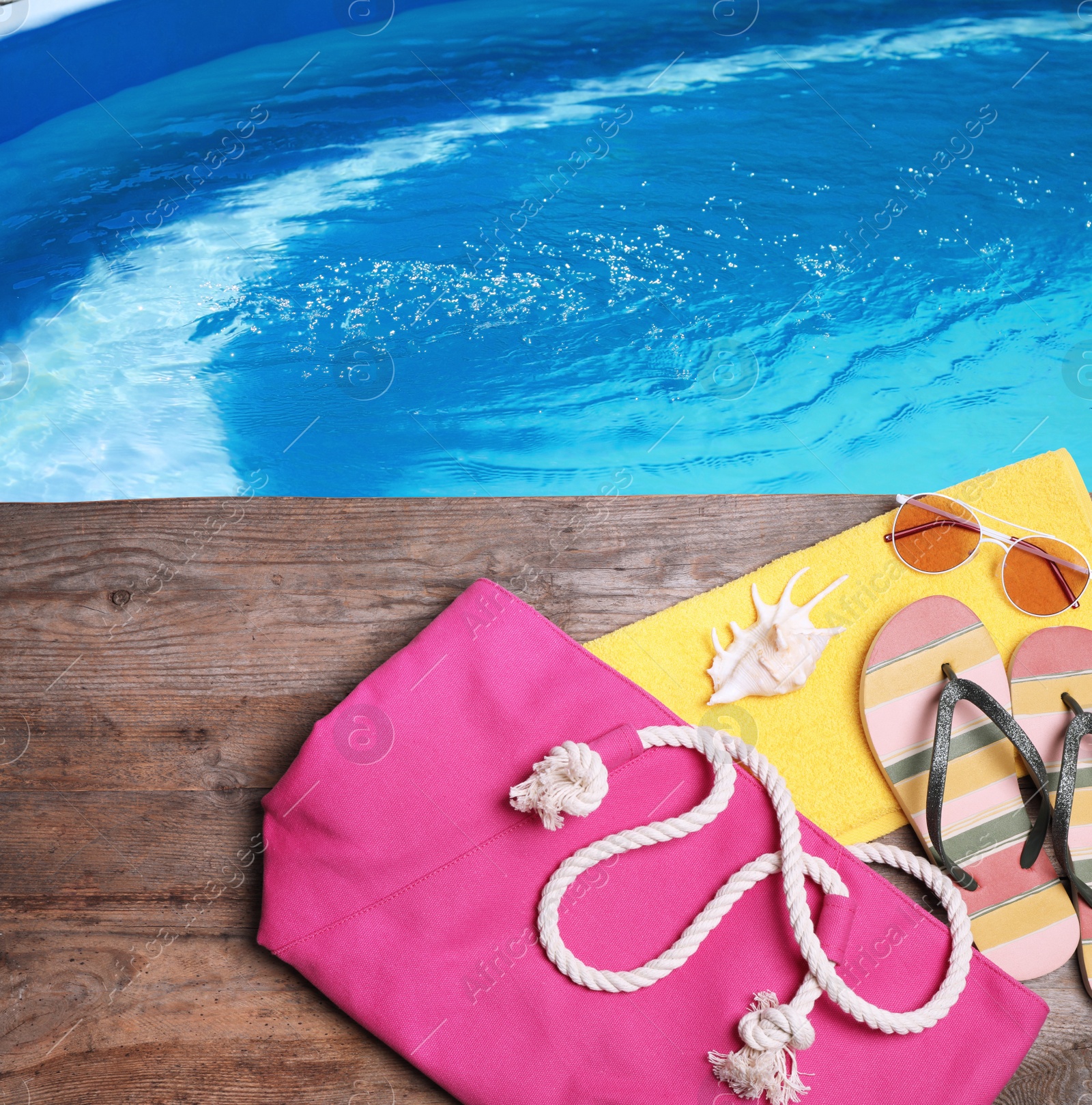 Image of Different stylish beach accessories on wooden surface near swimming pool, above view