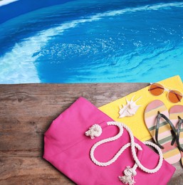 Image of Different stylish beach accessories on wooden surface near swimming pool, above view