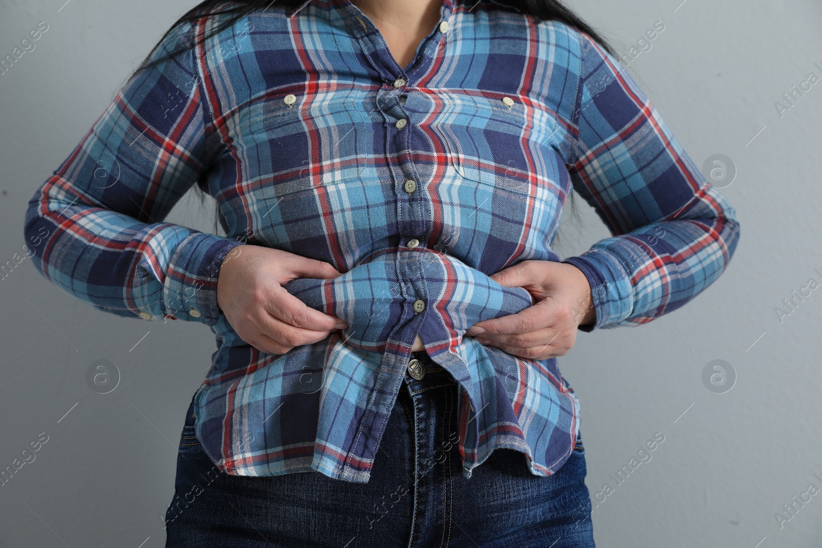 Photo of Overweight woman in tight shirt on light grey background, closeup