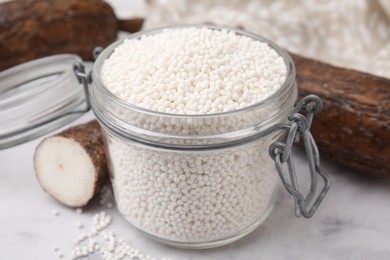 Tapioca pearls in jar and cassava roots on white table, closeup