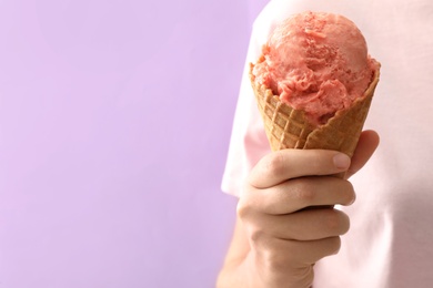 Photo of Woman holding pink ice cream in wafer cone on violet background, closeup. Space for text