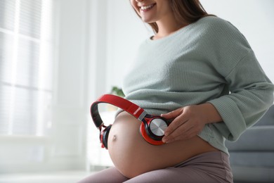 Photo of Pregnant woman with headphones on her belly indoors, closeup