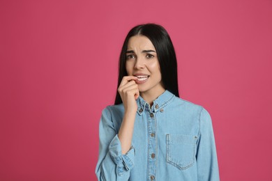 Photo of Young woman biting her nails on pink background. Space for text