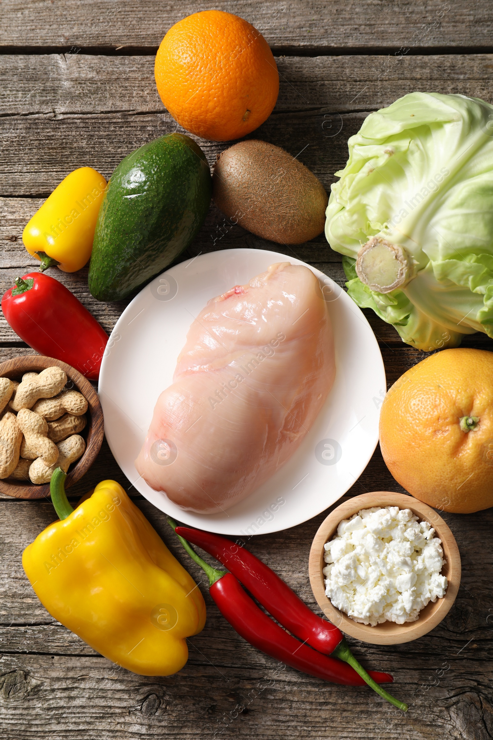 Photo of Healthy meal. Different vegetables and raw chicken breast on wooden table, flat lay