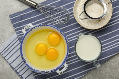 Photo of Whisk, eggs, milk and flour on grey table, flat lay