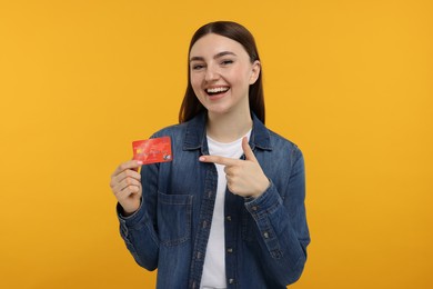 Happy woman pointing at credit card on orange background