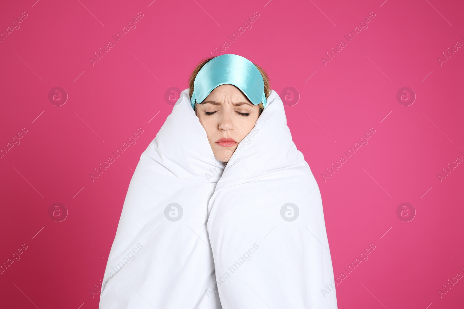 Photo of Young woman in sleeping mask wrapped with soft blanket on pink background