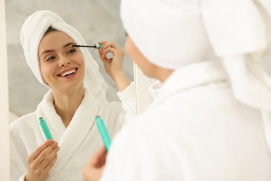 Beautiful woman applying mascara near mirror in bathroom