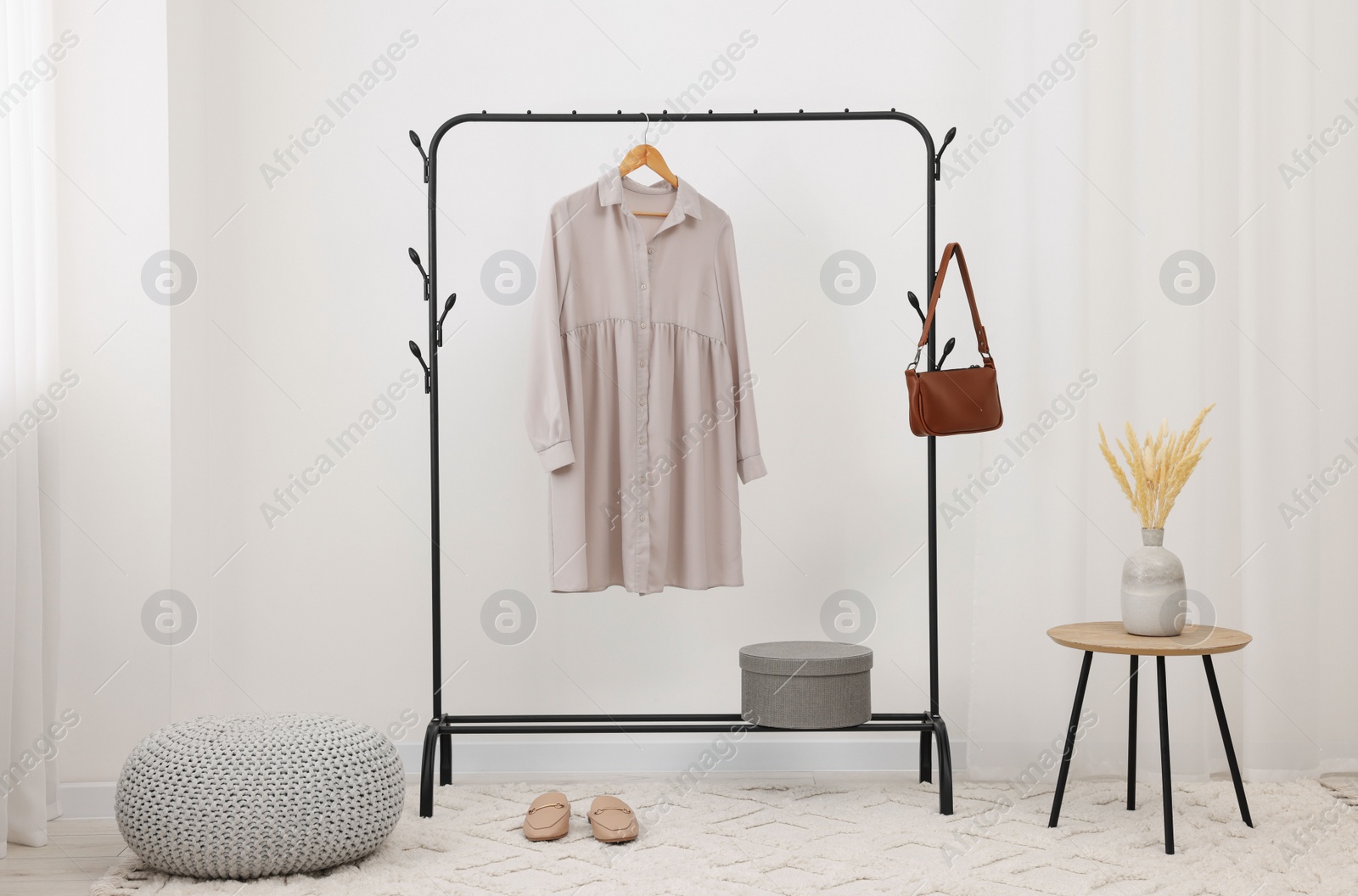 Photo of Clothing rack with stylish dress, bag and shoes in room