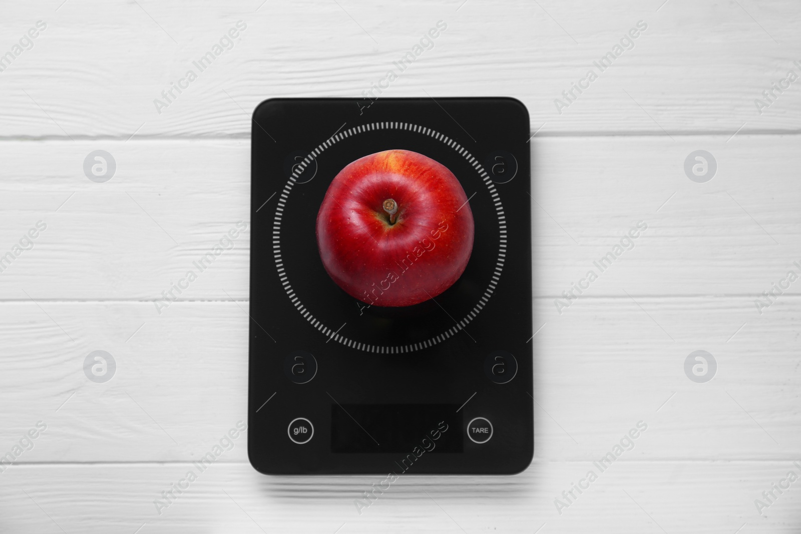 Photo of Digital kitchen scale with ripe red apple on white wooden table, top view