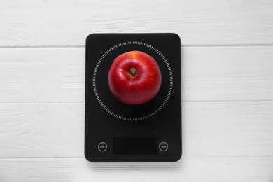 Digital kitchen scale with ripe red apple on white wooden table, top view