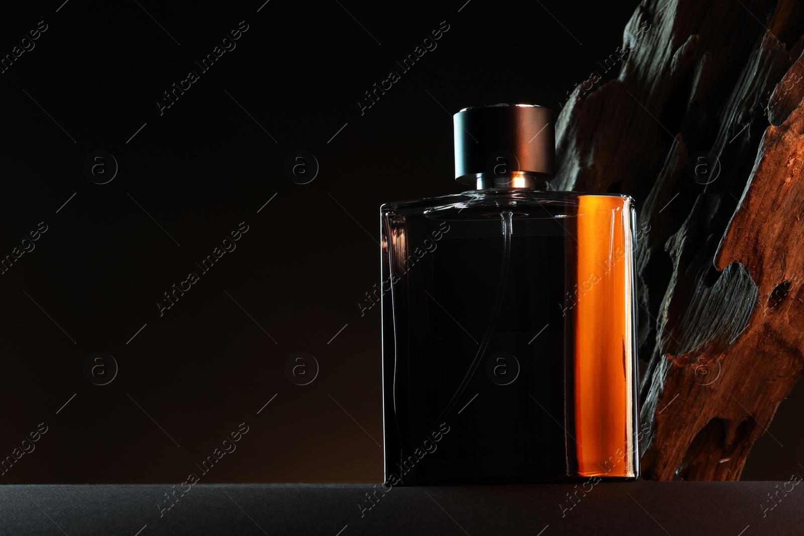 Photo of Luxury men`s perfume in bottle on grey table against dark background, space for text