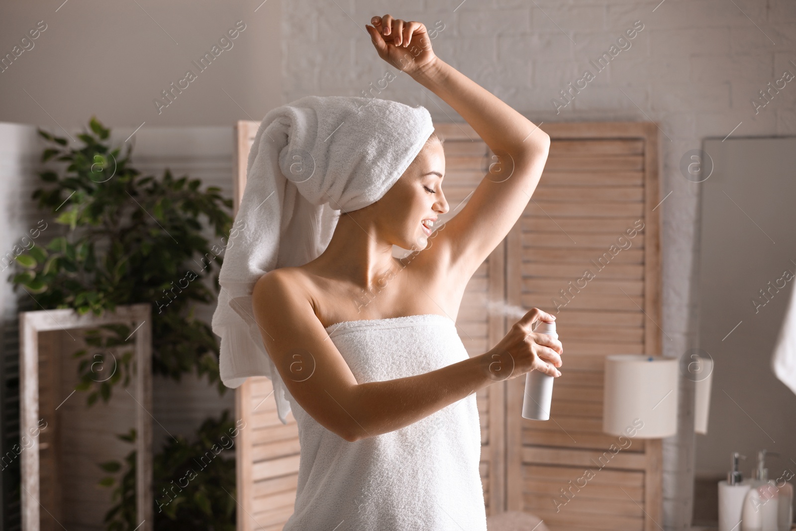 Photo of Beautiful young woman applying deodorant after shower in bathroom